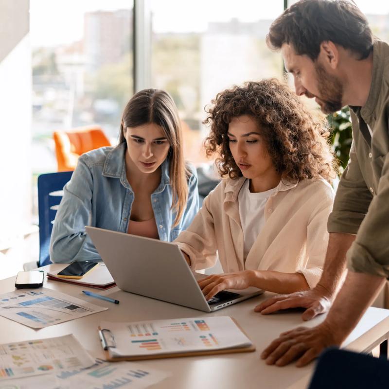 three team members gathered around a table looking at a laptop